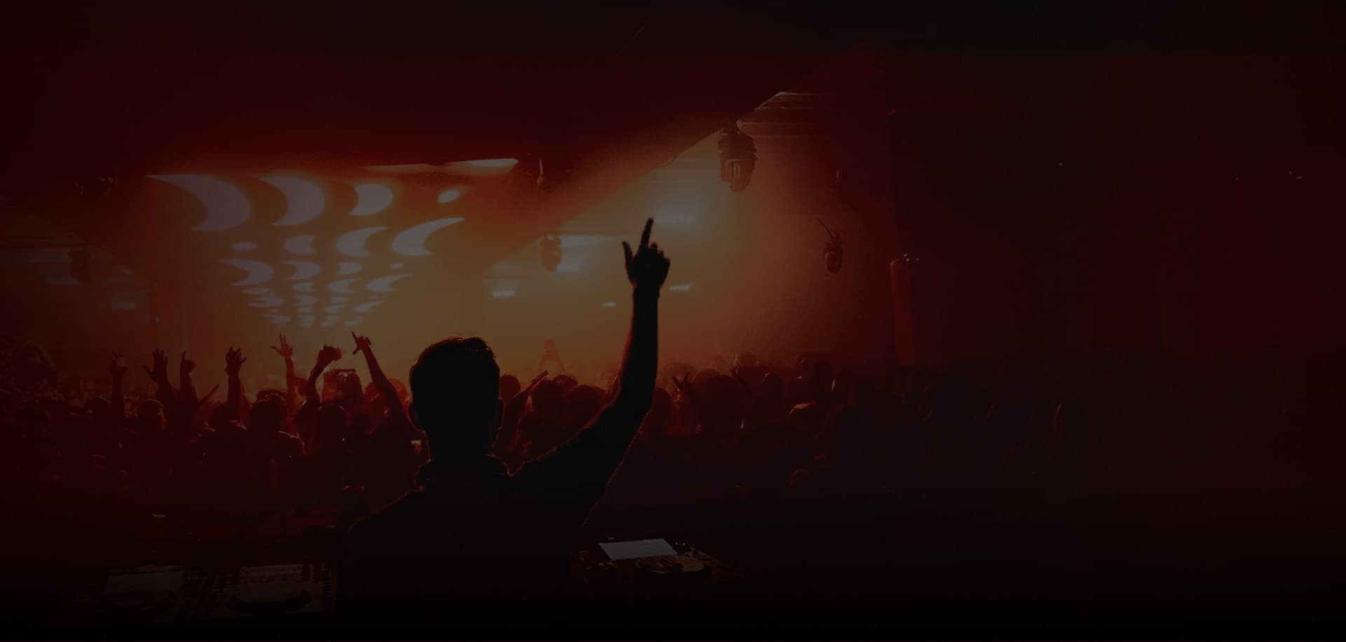 Un DJ en silhouette, bras levé devant la foule du club, sous une lumière rouge chaude.