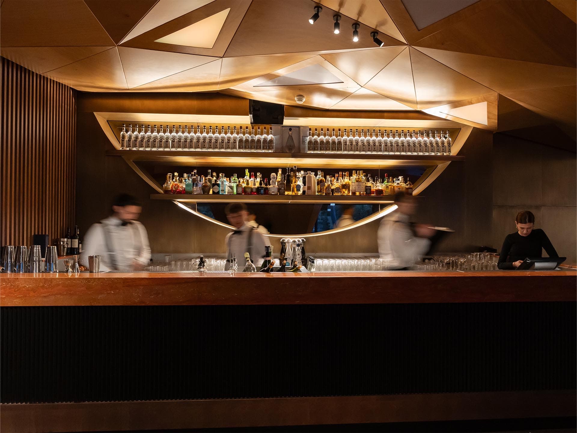Le bar de Twiga Monte-Carlo · plafond de bois à facettes, long comptoir rétroéclairé et bouteilles alignées
